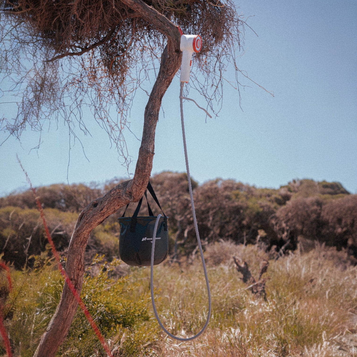 Niche Outdoors Portable Lithium Camp Shower and 10L Collapsible Bucket hanging off tree